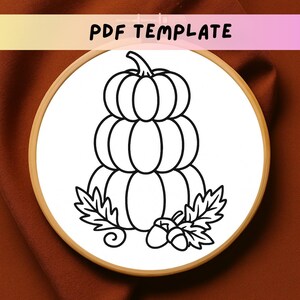 May include: A black and white embroidery design featuring a stacked pumpkin, leaves, and acorns. The design is set within a wooden embroidery hoop. The text "PDF TEMPLATE" is at the top.