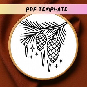 May include: A black and white embroidery design featuring pinecones, icicles, and stars, set within a wooden embroidery hoop. The text "PDF TEMPLATE" is displayed at the top. This design is perfect for crafting and home decor projects.