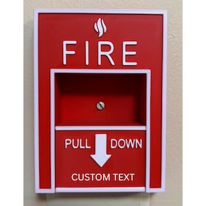 Peut inclure: Un déclencheur d'alarme incendie rouge avec le texte blanc « FIRE » en haut et « PULL DOWN » avec une flèche au milieu. Le bas de la station porte le texte « CUSTOM TEXT ». L'alarme a une bordure blanche.