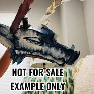 May include: A handcrafted dragon mask featuring a blue and white painted finish with prominent dark blue scales and sharp teeth. The mask includes large, textured, multi-colored antlers extending from the top. Text on the image reads NOT FOR SALE EXAMPLE ONLY.