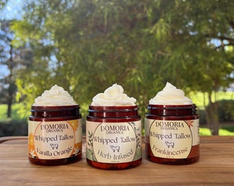 Può includere: Tre vasetti di vetro di sego montato con guarnizione di panna bianca. Ogni vasetto ha un'etichetta con il testo "DOMORIA ORGANICS Whipped Tallow" e un gusto: Vaniglia Arancia, Herb Infused e Frankincense. I vasetti sono su una superficie di legno.