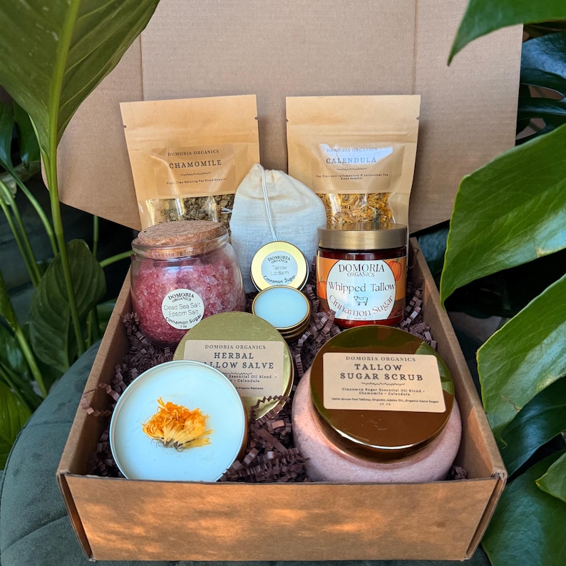 Puede incluir: Una caja de regalo llena de varios productos de cuidado personal. La caja contiene frascos de sal del Mar Muerto, az&uacute;car de canela de sebo batido y exfoliante de az&uacute;car de sebo. Tambi&eacute;n se incluyen sobres de manzanilla y cal&eacute;ndula, y ung&uuml;ento de sebo herbal.