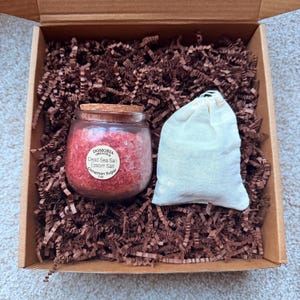 Puede incluir: Una caja de regalo que contiene un peque&ntilde;o frasco de vidrio con tapa de corcho, lleno de sal del Mar Muerto roja, sal de Epsom y az&uacute;car de canela. Tambi&eacute;n hay una peque&ntilde;a bolsa de tela blanca en la caja, llena de relleno de papel marr&oacute;n.