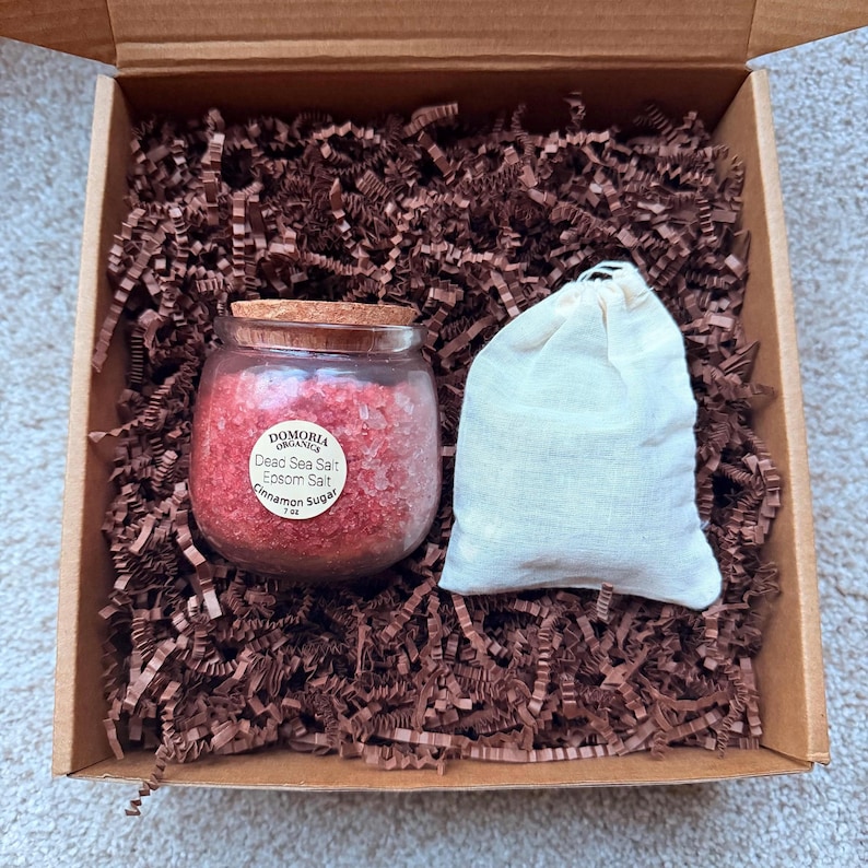 Puede incluir: Una caja de regalo que contiene un peque&ntilde;o frasco de vidrio con tapa de corcho, lleno de sal del Mar Muerto roja, sal de Epsom y az&uacute;car de canela. Tambi&eacute;n hay una peque&ntilde;a bolsa de tela blanca en la caja, llena de relleno de papel marr&oacute;n.
