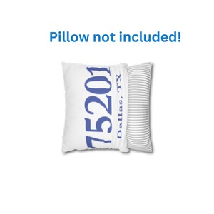 May include: White pillow with the blue text "75201 Dallas, TX". A second pillow with grey and white stripes is next to it. The text "Pillow not included!" is above the pillows.