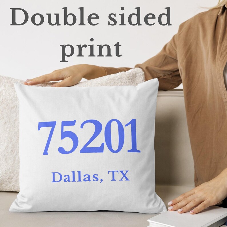 May include: White square cushion with the blue text "75201 Dallas, TX". The words "Double sided print" are above the cushion. The cushion is on a white surface.