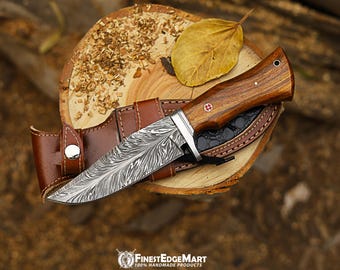 May include: A Damascus steel knife with a wooden handle and leather sheath. The blade has a unique pattern, and the handle is a warm brown color. The knife rests on a wooden surface with a dried leaf.