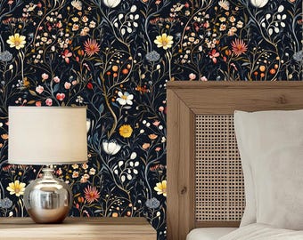 May include: A dark floral wallpaper featuring a repeating pattern of colorful flowers and foliage in shades of yellow, orange, pink, and white against a navy blue background. The image includes a wooden nightstand with a silver lamp and a bed frame.