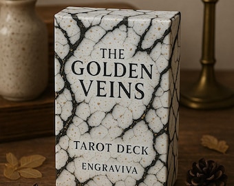 May include: A white box with black veins and gold flecks. The box has the text "The Golden Veins Tarot Deck Engravviva" printed on it.