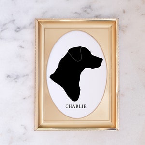 May include: A gold-coloured frame with a white oval mount and a black silhouette of a dog's head. The dog's name, "CHARLIE", is printed below the silhouette.