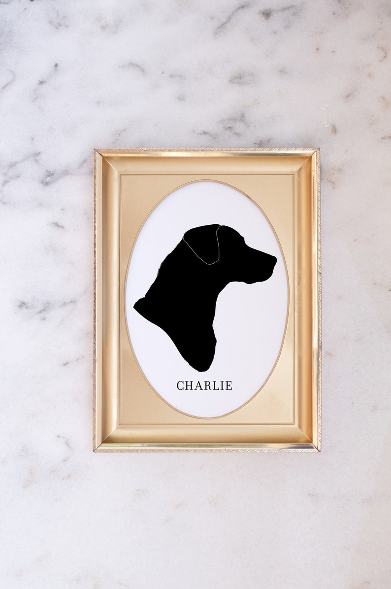 May include: A gold-coloured frame with a white oval mount and a black silhouette of a dog's head. The dog's name, "CHARLIE", is printed below the silhouette.