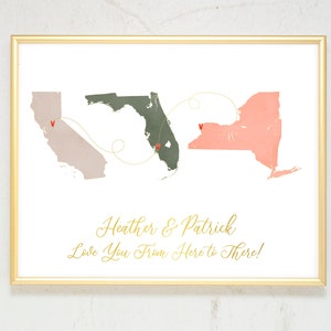 May include: A framed print with a gold frame featuring a map of the United States with a gold line connecting California, Florida, and New York. The text "Heather & Patrick Love You From Here to There!" is printed in gold lettering below the map.
