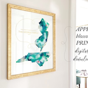 May include: A watercolour print of New Jersey and North Carolina with a gold line connecting the two states. The text "NEW JERSEY TO NORTH CAROLINA THE GEORGE FAMILY 2023" is written in gold lettering. The print is framed in a gold frame.