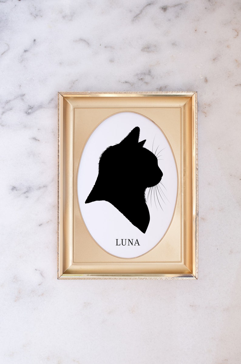 May include: A gold-coloured frame with a white oval mount and a black silhouette of a cat's head. The name "LUNA" is printed below the silhouette.