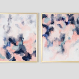 May include: Two abstract paintings in gold frames. The paintings are both pink, blue, and white with a watercolor effect.