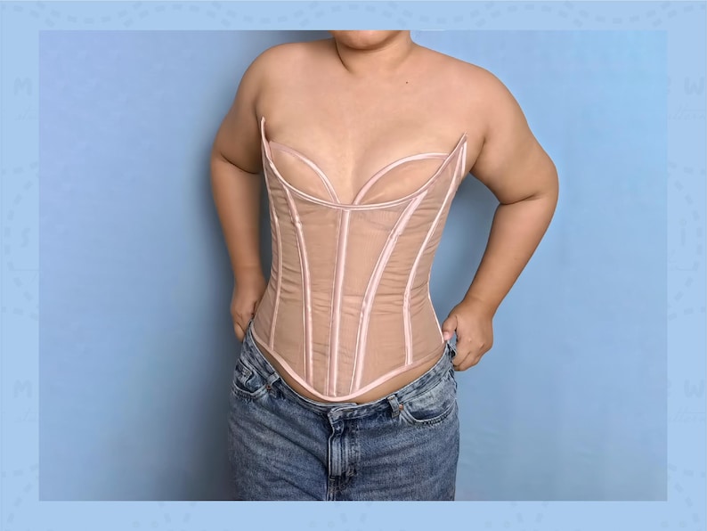 May include: A beige corset with a sheer overlay and pink trim. The corset has a structured design with vertical boning and a sweetheart neckline. The garment is worn with blue denim jeans. The background is a light blue.