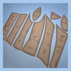 May include: A collection of brown paper corset pattern pieces, cut and arranged on a light blue surface. The pieces are labeled with text including "Athena Corset", measurements, and cutting instructions. The pattern pieces are for a corset.