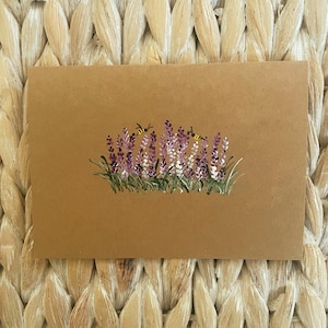 May include: A rectangular tan card featuring a hand-painted illustration of a cluster of purple and white lavender flowers with green stems and leaves. Two small yellow and black bees are depicted hovering near the top of the floral arrangement.