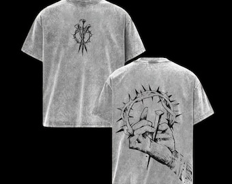 May include: Two gray t-shirts with black graphic designs. One shirt features a nail and thorn design, while the other displays a hand holding a nail and a crown of thorns. The shirts have a textured, vintage look.