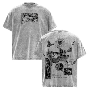 May include: Gray t-shirt with a distressed texture. The front features a black and white illustration of a face. The back displays a detailed graphic with birds, a sun, and the text "THE SHATTERING DOWNFALL OF PRIDE."