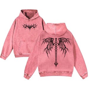 May include: Pink hooded sweatshirt with a front pocket and a black graphic design on the front and back. The back design resembles a spine with wing-like extensions. The sweatshirt has a washed, vintage look.