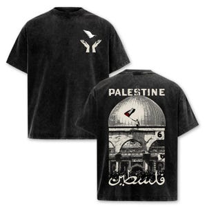May include: A black acid-wash t-shirt featuring a white graphic of hands releasing a dove on the front. The back displays a detailed illustration of a domed building, a person holding a flag, the text PALESTINE, the number 6, and Arabic script.