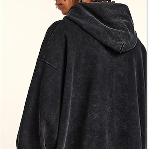 May include: A black, oversized hoodie with a faded, vintage wash effect. The hoodie features a large hood and a relaxed fit, perfect for casual wear. The fabric appears soft and comfortable, with a slightly textured appearance.