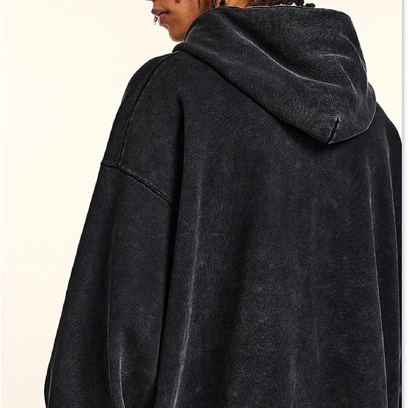 May include: A black, oversized hoodie with a faded, vintage wash effect. The hoodie features a large hood and a relaxed fit, perfect for casual wear. The fabric appears soft and comfortable, with a slightly textured appearance.
