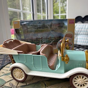 May include: A vintage-style toy car in pastel blue, brown, and cream. The toy car has a classic open-top design with detailed seating and wheels. The car is a miniature replica of a classic automobile.
