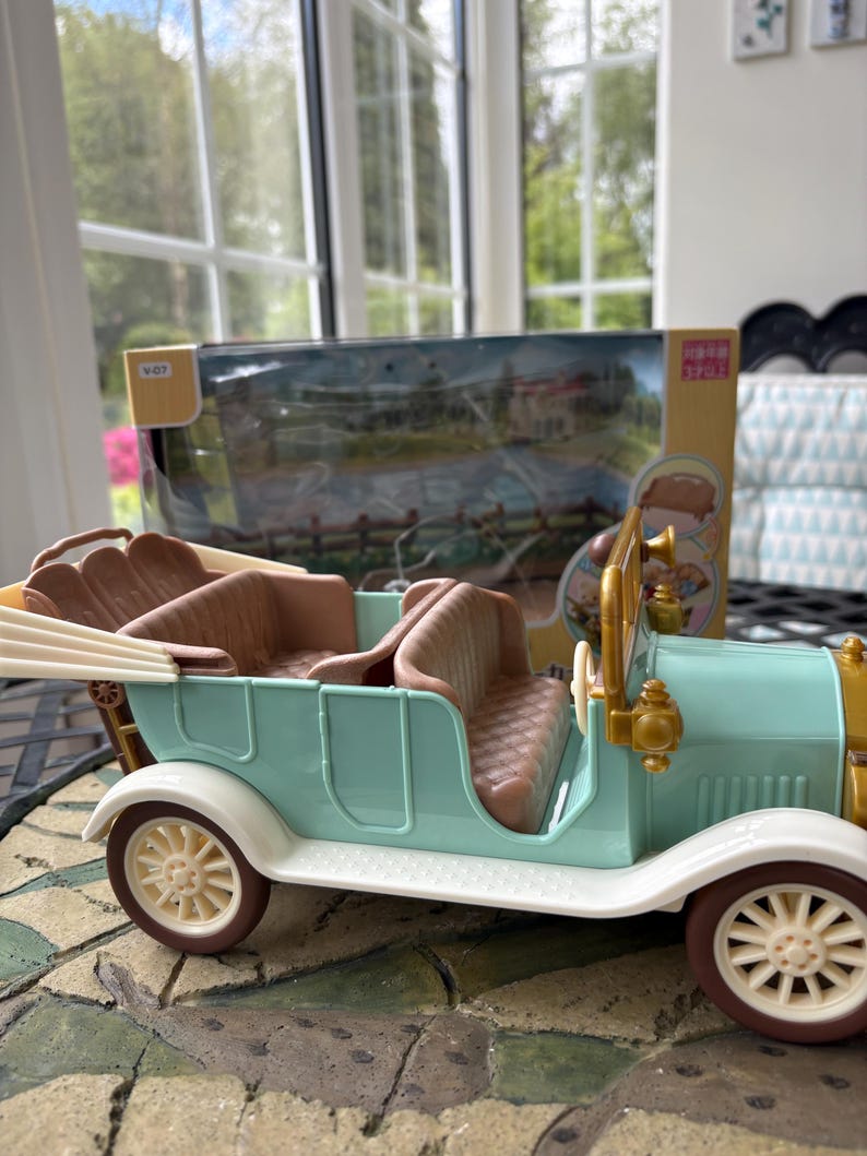 May include: A vintage-style toy car in pastel blue, brown, and cream. The toy car has a classic open-top design with detailed seating and wheels. The car is a miniature replica of a classic automobile.