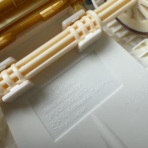 May include: Close-up of a toy carriage with a cream-colored body and wheels. The carriage has a gold-colored top and cream-colored axles. The text "MADE IN CHINA" and "EPOCH CO., LTD." are visible.