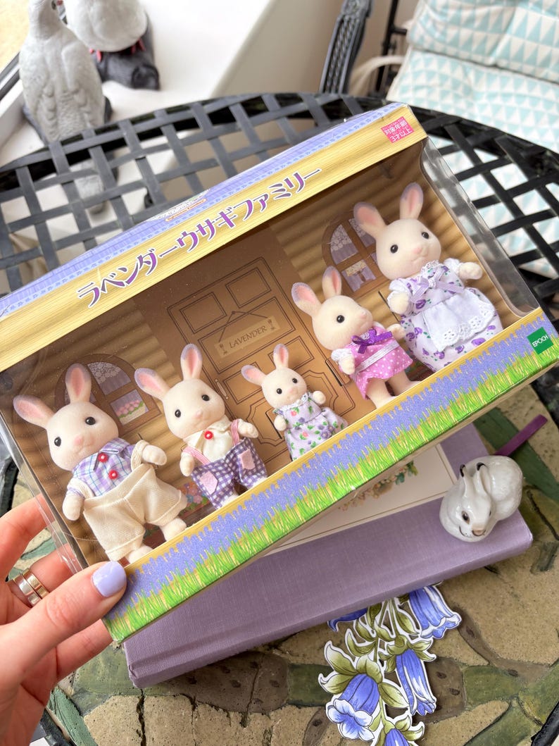 May include: A boxed set of toy rabbit figures, the Lavender Rabbit Family, with the Japanese text "ラベンダーウサギファミリー" on the box. The rabbits are dressed in various outfits, including dresses and overalls. The box has a lavender and green design.
