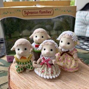 May include: A collection of Sylvanian Families sheep figures. The sheep are wearing various outfits, such as dungarees and dresses. The packaging is visible, displaying the words "Sylvanian Families".
