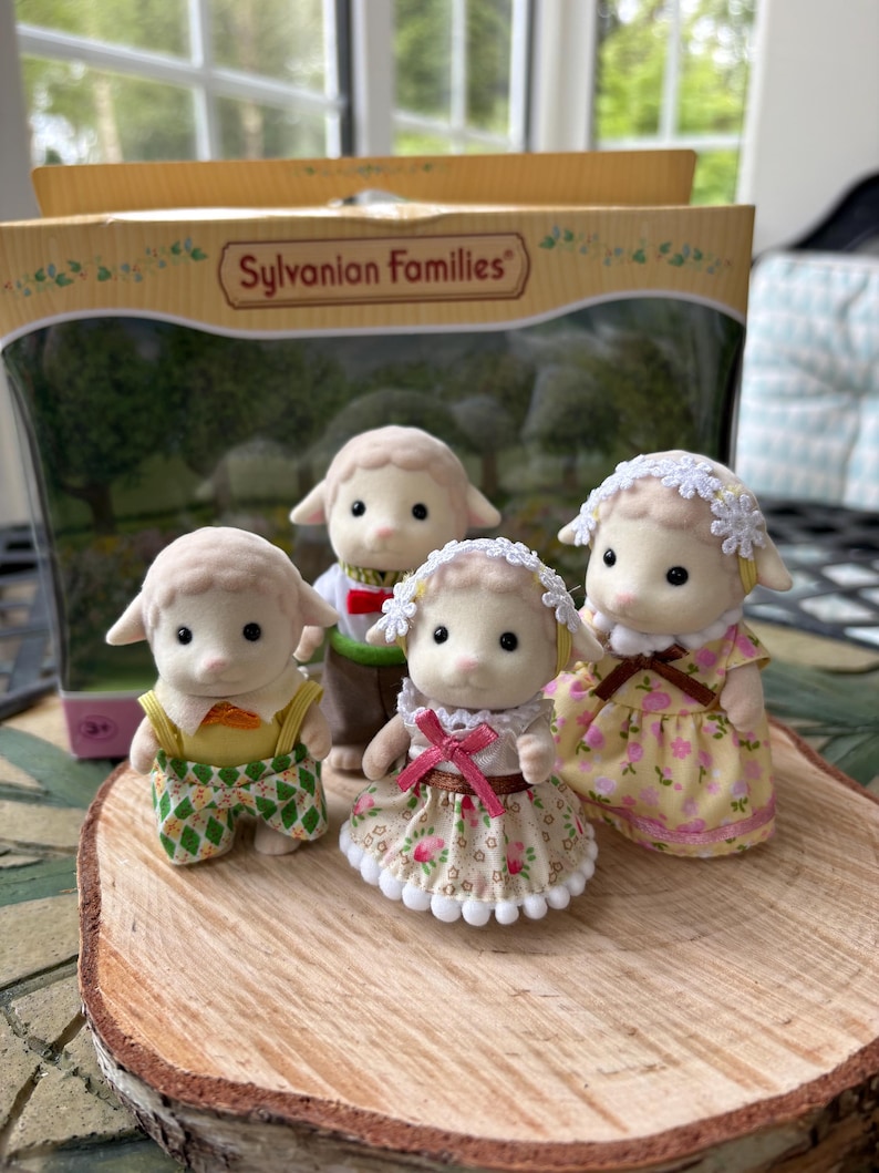 May include: A collection of Sylvanian Families sheep figures. The sheep are wearing various outfits, such as dungarees and dresses. The packaging is visible, displaying the words "Sylvanian Families".