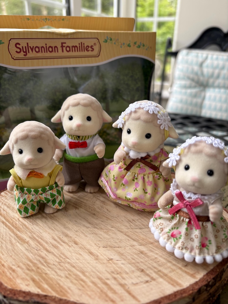 May include: Four Sylvanian Families sheep figures, each dressed in different outfits. One wears a green and yellow outfit, another a bow tie and vest, and two wear floral dresses. The figures are displayed on a wooden surface.