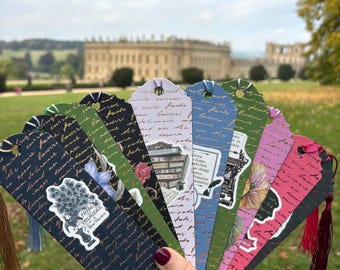 May include: A selection of decorative bookmarks with tassel details, showcasing literary themes and quotes. Each bookmark features distinct designs, including floral illustrations, book stacks, and script lettering. The bookmarks are held in front of a blurred outdoor background.