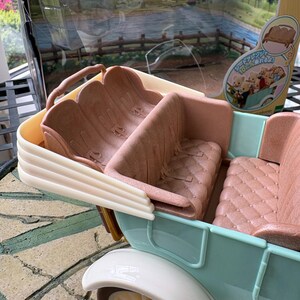 May include: A light blue and white toy car with brown seats. The car has a vintage design with a cream-colored wheel and a detailed interior. The packaging is visible in the background.