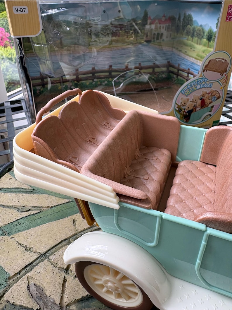 May include: A light blue and white toy car with brown seats. The car has a vintage design with a cream-colored wheel and a detailed interior. The packaging is visible in the background.