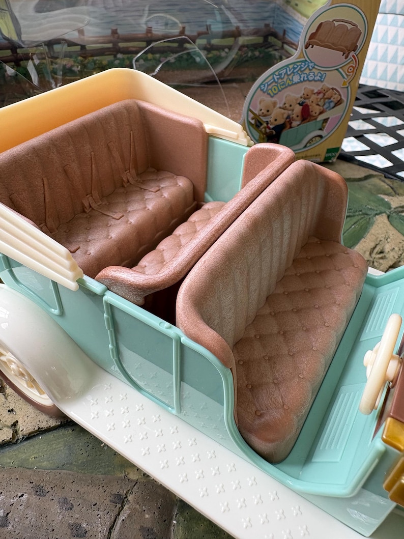 May include: A pastel blue and white toy car with brown seating. The car has a detailed interior with a steering wheel and a decorative exterior. The seats are a quilted brown color. The car is a toy.