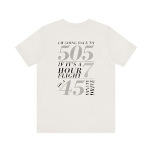 May include: White t-shirt with black text that reads "I'm going back to 505 if it's a hour flight or a 45 minute drive."