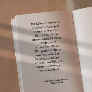May include: An open book with Dutch text discussing self-discovery after a difficult relationship. The book is titled "Dit helende boekje" and written by Riekie Smit. The pages are off-white, with a soft, neutral background.