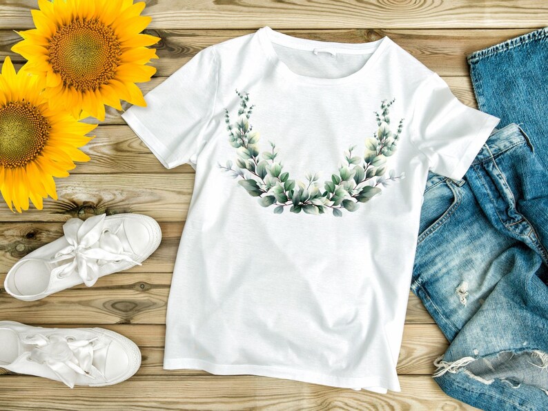 May include: White t-shirt with a watercolor eucalyptus leaf design. The shirt is paired with blue denim jeans and white sneakers. Two sunflowers are placed on a wooden surface.