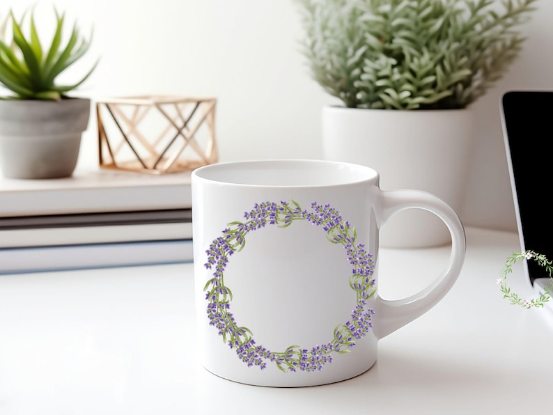 May include: White ceramic mug featuring a lavender wreath design. The wreath is composed of purple lavender flowers and green leaves, arranged in a circular pattern. The mug has a curved handle and is set against a bright background.