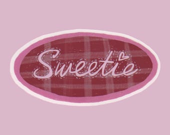 May include: A pink background with an oval-shaped design. The design features a maroon plaid pattern, a white border, and the word "Sweetie" in cursive with a small heart. The overall aesthetic is cute and feminine.