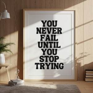 May include: A framed print with the motivational quote, "YOU NEVER FAIL UNTIL YOU STOP TRYING," in bold black letters. The print is set against a white background, framed in light wood, and displayed in a room with wooden paneling and natural light.