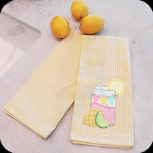May include: Two yellow gingham kitchen towels. One towel features an embroidered design of a mason jar filled with lemonade, a lemon slice, and a lime wedge.