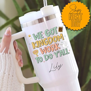 May include: White travel mug with a handle, featuring the text "WE GOT KINGDOM WORK TO DO Y'ALL" in colorful lettering. The design includes religious symbols and the name "Lily" in script. The mug has a white lid and a straw.
