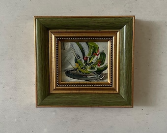 May include: A small framed painting of a green plant with red flowers in a black pot. The frame is green with gold trim.