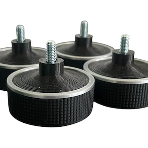 May include: Four black furniture feet with a textured, cylindrical base and a silver rim. Each foot has a threaded metal stud extending upwards. The feet are designed for furniture support and stability.