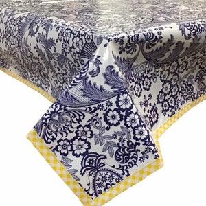 May include: White tablecloth with a blue and white floral pattern and a yellow gingham border. The tablecloth is made of vinyl and is waterproof.